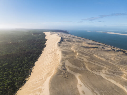 Aerial view of the stark contrast between the lush green forest and the towering, sandy Dune du Pilat against the deep blue sea, La Teste de Buch, Nouvelle-Aquitaine, France.