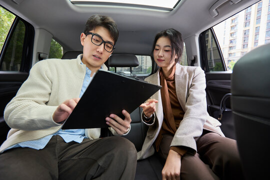 A businessman and businesswoman converse in the back seats of a car
