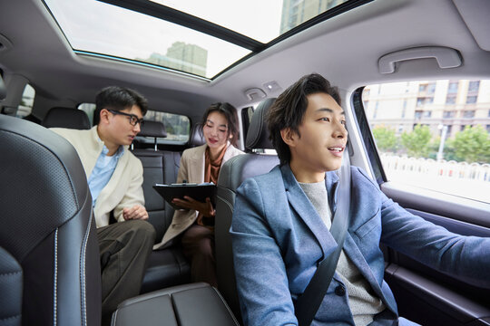A businessman and businesswoman converse in the back seats of a car