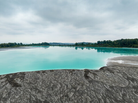 Aerial view of a vibrant turquoise lake contrasting with dark, textured shores, under a cloudy sky, Tuzla, Bosnia and Herzegovina.