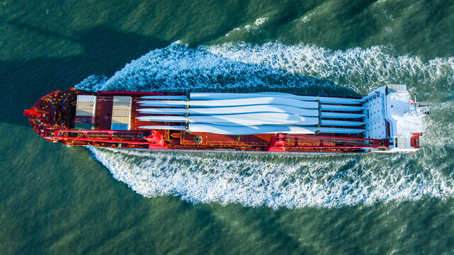 Aerial view of a vast cargo ship cutting through the water, carrying wind turbine blades creating a striking contrast against the deep blue sea, Freeport, Texas, United States.
