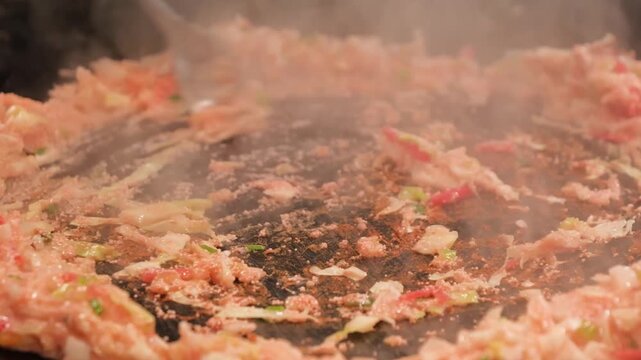 Close-up footage of monjayaki, a savory pan-fried batter dish, being prepared on a teppan griddle. The scene shows the characteristic gooey texture and steam rising as the mixture of dashi-based batte