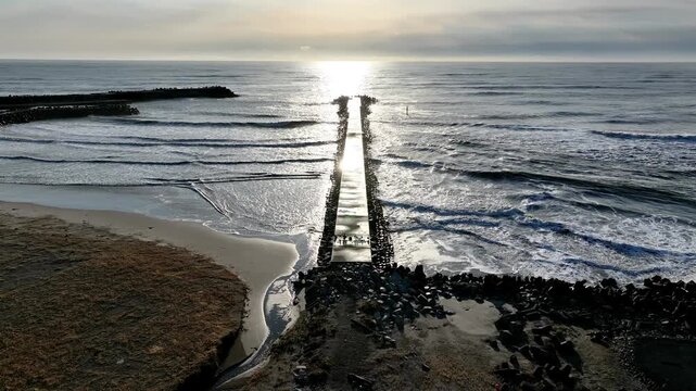 Aerial view of breakwater walkway leading toward sunrise over the ocean, Tomioka Fukushima