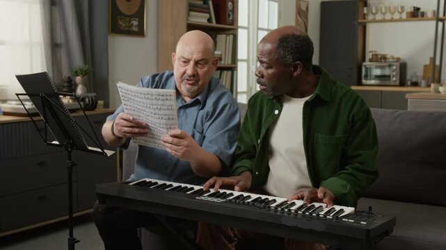 Medium shot of middle aged music teacher explaining notes and melody to senior African American man learning to play piano in lesson Useful for music education platforms or course landing pages