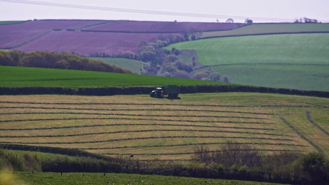 Tractor in harvested field, rolling countryside in Cornwall, UK