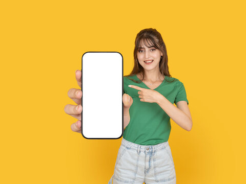 Smiling young woman pointing at smartphone mock up screen presenting mobile app. Isolated on bright yellow background with copy space, perfect for advertising, promotion or digital service concept.