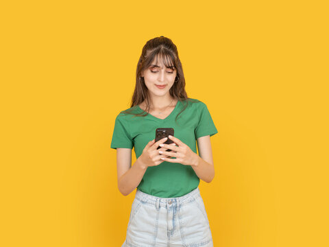 Young woman using smartphone with calm focused expression while typing message. Isolated on bright yellow background with copy space, ideal for mobile communication or lifestyle concept idea image.
