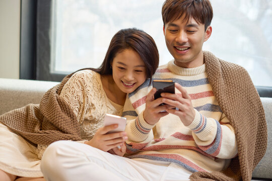 Young couple relax together on the couch, scrolling through their phones