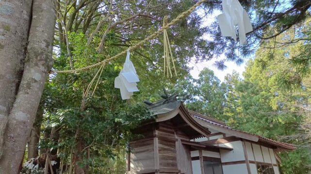 Traditional Japanese shrine seen through sacred rope in rural forest setting