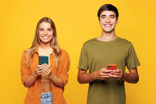 Young smiling happy cheerful couple two friends family man woman wear casual clothes hold in hand use mobile cell phone together isolated on pastel plain light yellow color background studio portrait.
