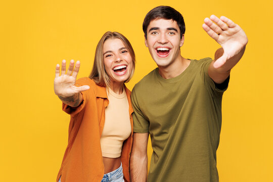 Young fun happy couple two friends family man woman they wear casual clothes together hug spread hands pov invite saying welcome isolated on plain yellow background studio portrait. Lifestyle concept.