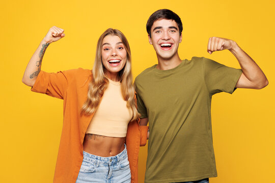 Young couple two friends family man woman wears shirt casual clothes together showing biceps muscles on hand demonstrating strength power isolated on plain yellow background studio. Lifestyle concept.