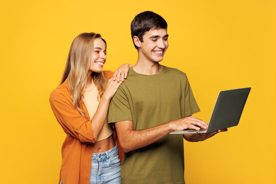 Sideways young happy couple two friends family IT man woman wearing casual clothes hold use work on laptop pc computer together isolated on pastel plain light yellow color background studio portrait.