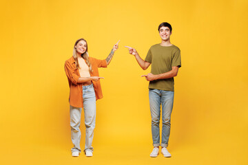 Fototapeta premium Full body fun young couple two friends family man woman wear casual clothes together point index finger between them on workspace area mock up isolated on pastel plain yellow color background studio.