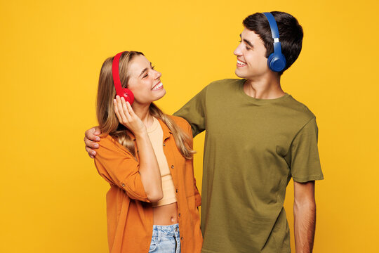 Young fun happy couple two friends family man woman wear shirt casual clothes together listen music in headphones isolated on pastel plain light yellow background studio portrait. Lifestyle concept