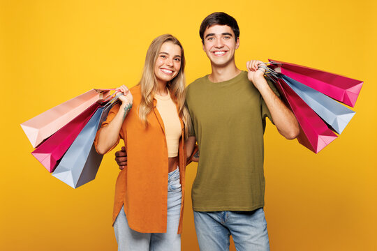 Young happy couple friends family man woman they wear casual clothes together hold shopping paper package bags isolated on plain yellow background studio portrait. Black Friday sale buy day concept.