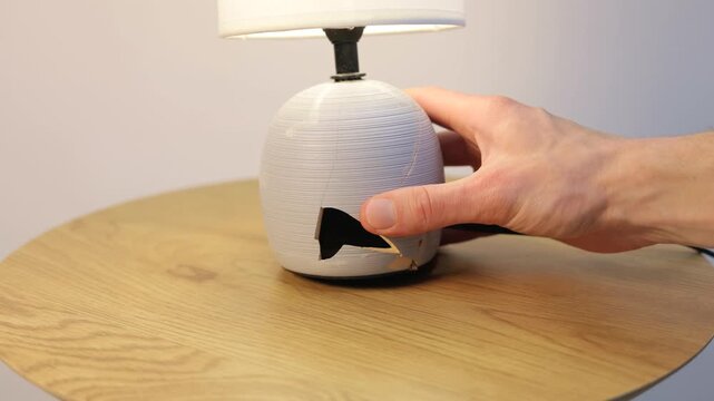 Close-up of a broken ceramic lamp base on a wooden table, emphasizing fragility, damaged household items, and repair concepts.