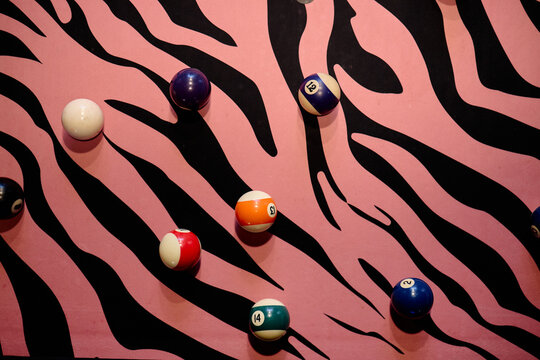 Overhead view of billiard balls resting on pink zebra pattern surface, creating playful gaming concept. Suitable for entertainment marketing, nightlife promotion, leisure branding
