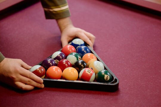 Close up of young adult hands arranging billiard balls in rack on pool table, preparing game and competition concept. Suitable for leisure marketing, sports venue promotion, recreation ads
