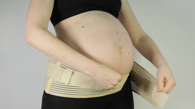 Pregnant woman putting on a supportive maternity belly band for back relief and comfort during pregnancy, close-up.