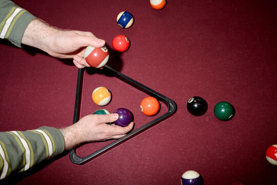 Overhead shot of middle aged man arranging billiard balls in rack on pool table, preparing game setup. Suitable for leisure marketing, bar promotion, recreation concepts
