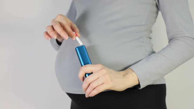 Pregnant woman holding tobacco heating device with a stick, highlighting the controversial and harmful habit of smoking or vaping during pregnancy.