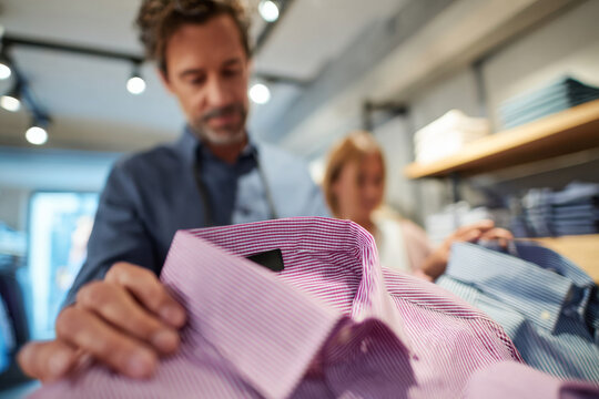 Studio lighting featuring man comparing two shirts while shopping with friend in modern clothing boutique, bright stylish retail interior, clean contemporary design, natural shopping atmosphere, in