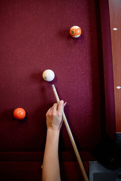 Vertical shot of young adult woman hand aiming cue stick at billiard balls on pool table, preparing strategic shot. Suitable for leisure marketing, gaming venues, competition content
