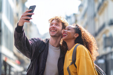 Fototapeta premium Stylized man taking selfie with friend while walking in city street, both laughing and looking at smartphone, bright natural daylight, modern urban background softly blurred, composition for business
