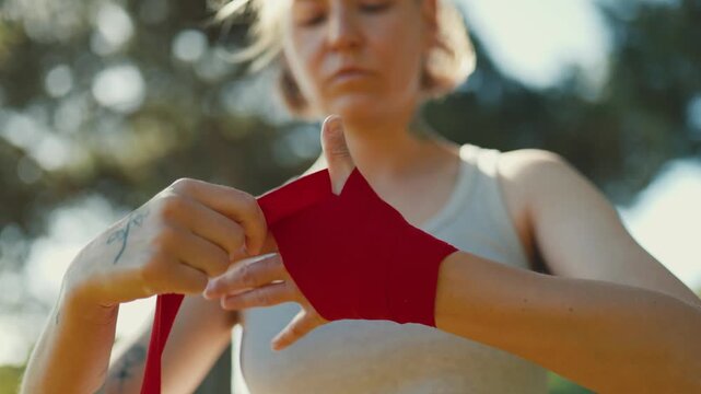 Woman fighter wrapping hands with red bandages outdoors