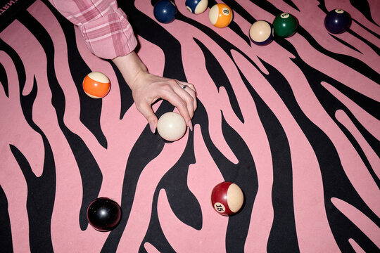 Close up of Caucasian woman hand positioning cue ball on billiards table with bold animal print felt, suggesting playful leisure branding. Useful for nightlife, entertainment, gaming promotion
