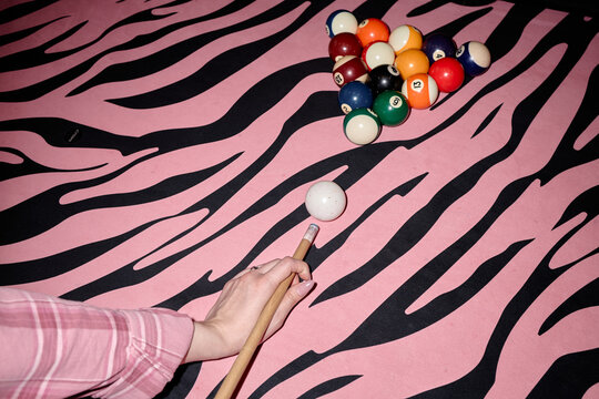 Caucasian woman hand aiming cue ball toward racked billiard balls on patterned pool table, showing leisure gaming and nightlife concept. Ideal for entertainment marketing and venue promotion
