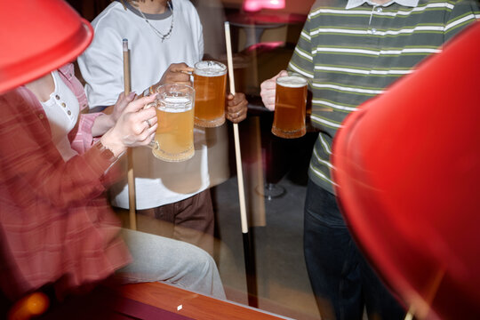 Young adults holding beer mugs and pool cues, socializing during billiards game in bar. Image supporting nightlife marketing, leisure promotion, friendship or entertainment campaigns
