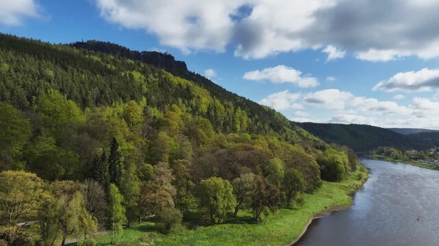 Scenic aerial view of the Elbe valley in Saxon Switzerland with densely forested hills and the Elbe river under a blue cloudy sky in spring.