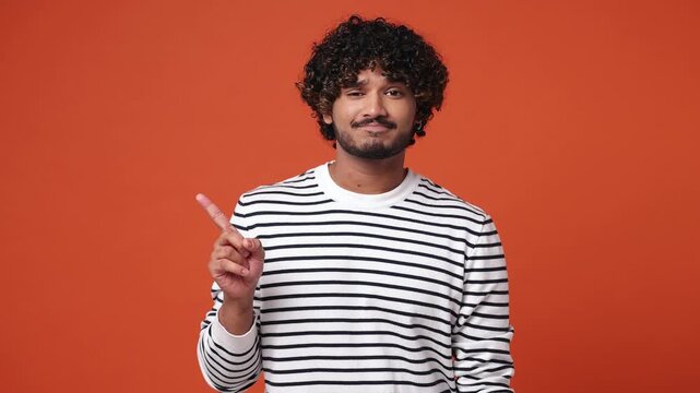Young fun Indian man wear striped sweatshirt casual clothes show finger gesture no I do not need it point thumb down dislike gesture isolated on plain orange red background studio. Lifestyle concept