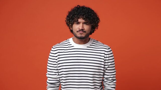 Young mad stressed dissatisfied upset Indian man wear striped sweatshirt casual clothes spread hands scream shocked look camera isolated on plain orange background studio portrait. Lifestyle concept