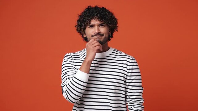 Excited smart puzzled pensive young Indian man wear striped sweatshirt casual clothes look around think scratches at temple comes up with idea raise finger get plan isolated on plain orange background