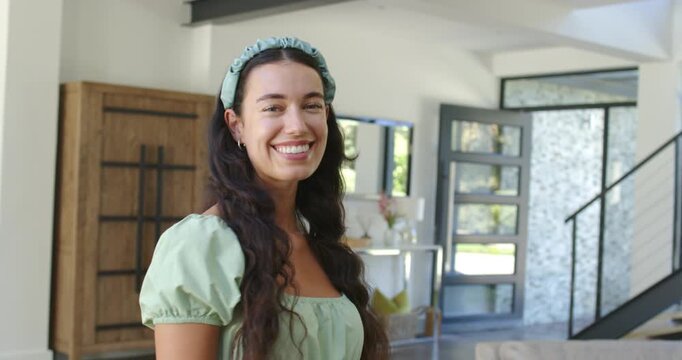 Adult woman posing in entry holding gentle smile, widening into laughter and wearing green headband