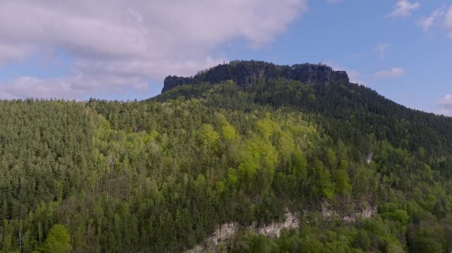Aerial view of the Lilienstein mountain in Saxon Switzerland with dense green forests and striking rock formations under a blue cloudy sky.