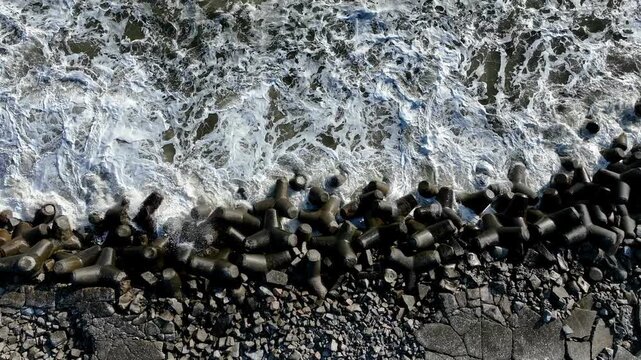 Aerial top-down view of waves crashing onto tetrapods at coast, Tomioka Fukushima