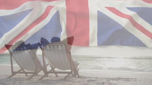 Senior couple sitting in chairs facing sea, Union-Jack overlay animation waving, promoting tourism