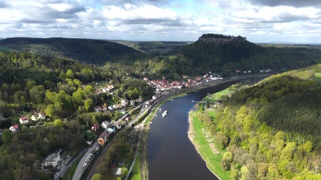 Wide aerial panorama of the Elbe river near Koenigstein in Saxon Switzerland, featuring the fortress, forested valleys, and the town under a dramatic cloudy sky.