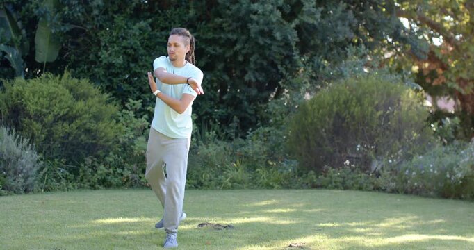 Man starting relaxed on lawn, stretching then rotating arms for balance wearing mint tee and watch