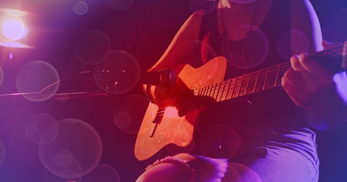 Strumming teen playing acoustic guitar on dim stage, mic stand, red purple lights, ripped shorts