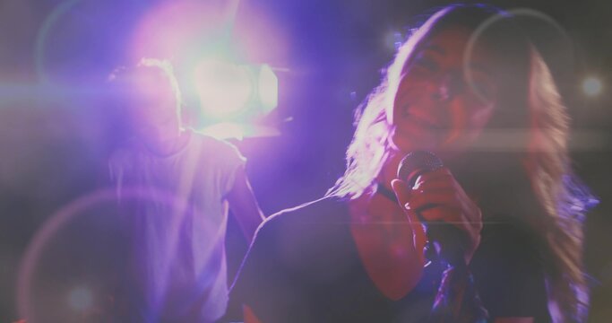 Singing lead singer in V-neck holding mic onstage with pink spotlights lens flares haze, copy space
