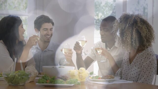 Four adults raising wine glasses at wood table, lens bokeh softening over food, celebrating meal