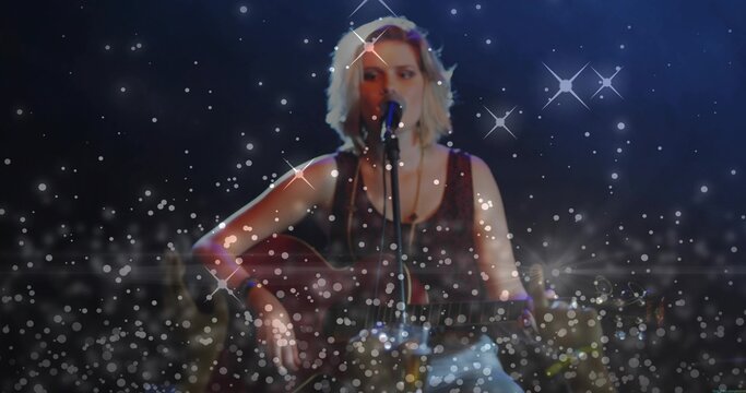 Singing teen strumming acoustic guitar center-stage, in dark tank top and light jeans into mic