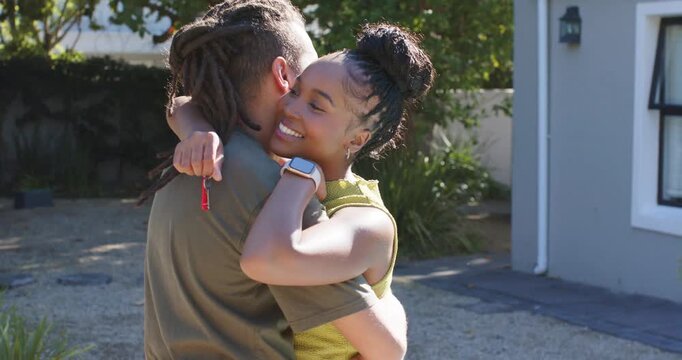 Couple embracing on driveway, woman in green top holding red key fob, reuniting after arriving home