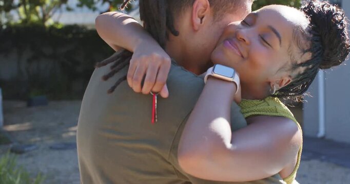 African American couple hugging in driveway, woman holding red key behind partner's back, smiling