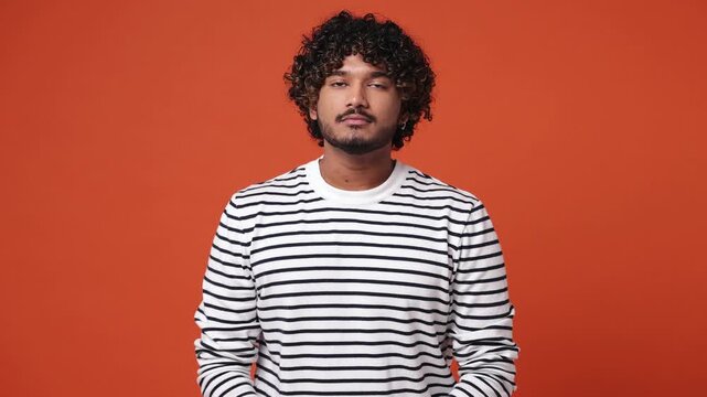 Spiritual tranquil happy young Indian man wears striped sweatshirt casual clothes hold spreading hands in yoga om aum gesture relax meditate try to calm down isolated on plain orange red background